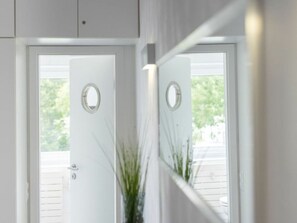 Una puerta blanca con un espejo circular encima que refleja una vista de una cubierta de madera y follaje exterior.