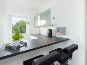 Eine moderne Küche mit schwarzem Arbeitsplatz, zwei schwarzen Barhocker, einer Kaffeemaschine und einem Blumentopf.