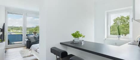 Cocina moderna con encimera negra, dos taburetes de bar, una planta en maceta y vistas al exterior a través de grandes ventanales.