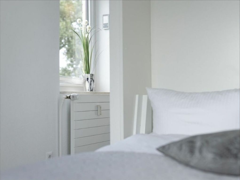 Ein Schlafzimmer mit Bett, Heizkörper und Fenster mit Blick auf Bäume.
