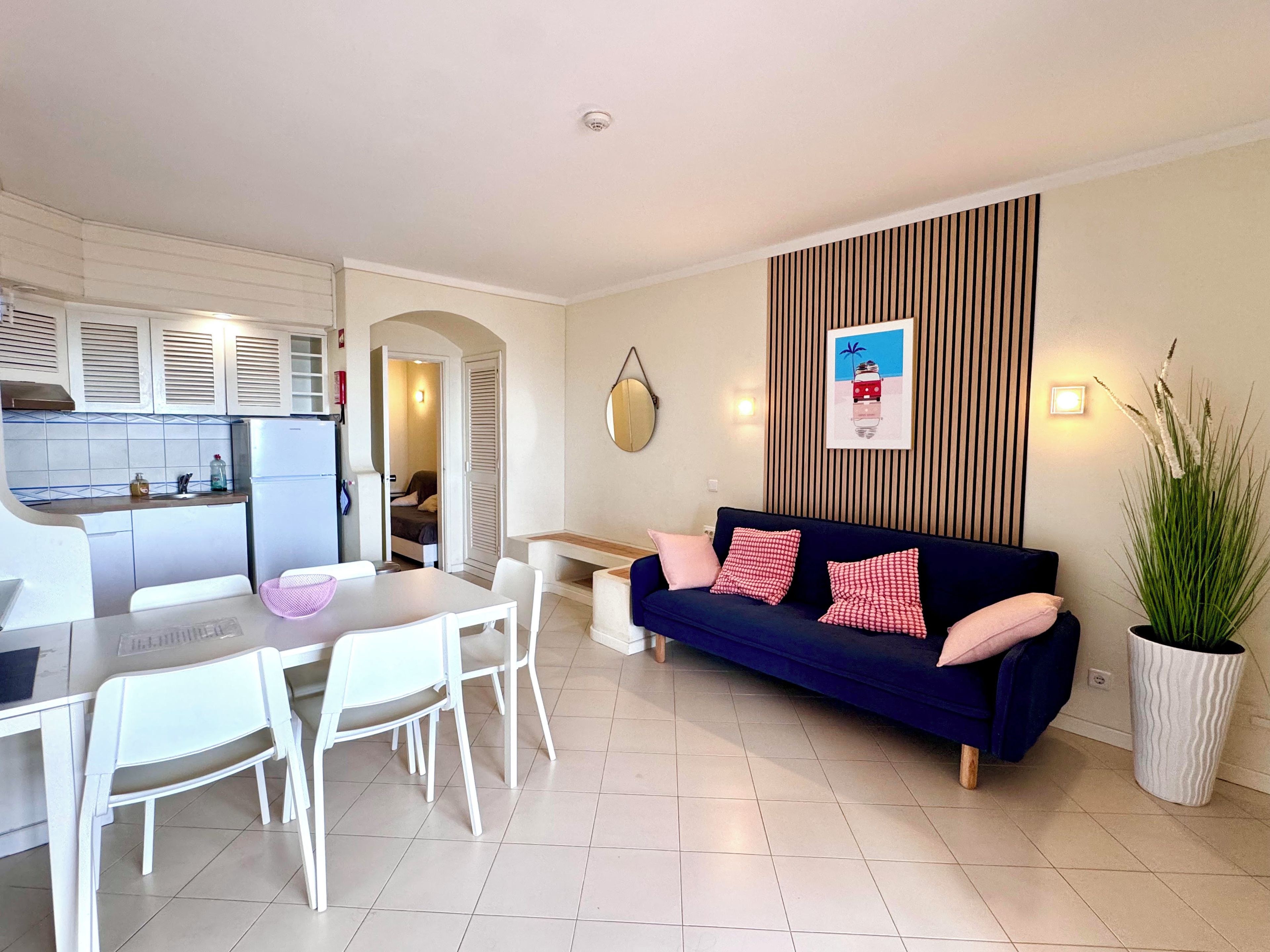 A compact living space with a kitchenette, a dining area, a sofa, and a potted plant.