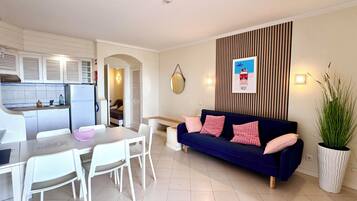 A compact living space with a kitchenette, a dining area, a sofa, and a potted plant.