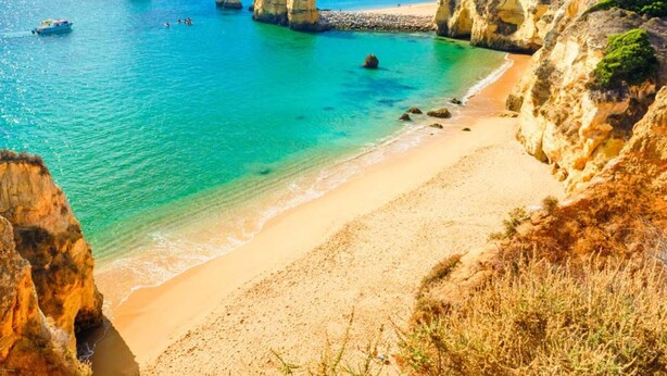 Une plage côtière aux eaux turquoise et limpides, bordée de falaises rocheuses et d’un rivage sablonneux.