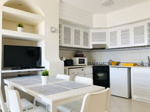 Une cuisine moderne avec des meubles blancs, un four encastré, un four à micro-ondes et un coin repas comprenant une table et des chaises.