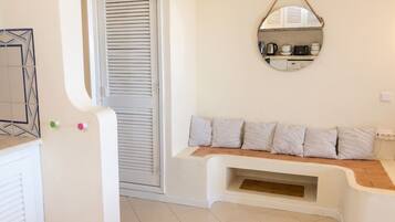 A room with a white door, a bench with checkered cushions, a wall-mounted mirror, and a tiled floor.