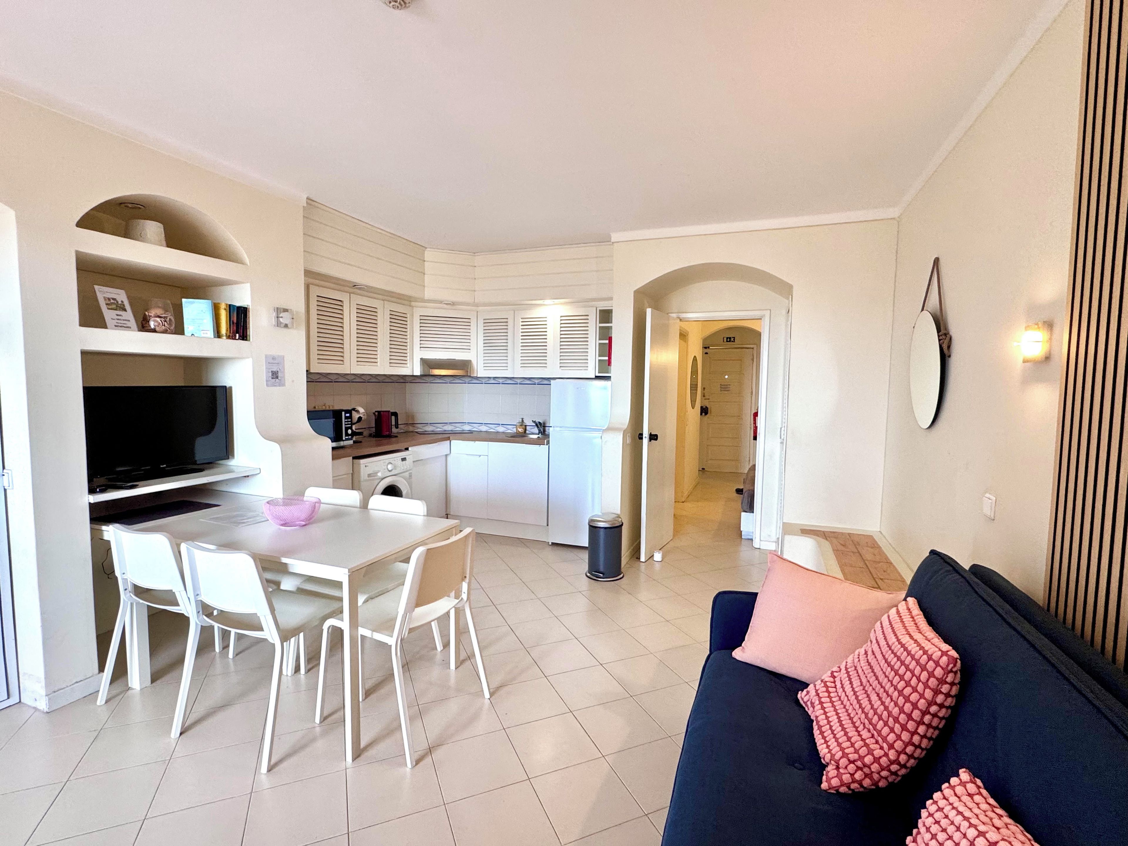 A compact living space with a kitchenette, dining area, and a sofa with decorative pillows.