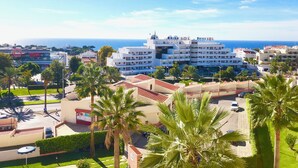 Un hôtel situé sur la côte, composé de plusieurs bâtiments blancs, bordé de palmiers et offrant une vue sur la mer.