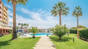 Un espace piscine avec un ciel dégagé, des palmiers et un chemin menant à un bâtiment.
