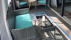 Een balkon met rieten meubels, een glazen deur en een schilderij aan de muur.
