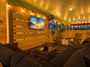Un coin salon accueillant avec un grand canapé, une petite table ornée d’une plante et un téléviseur fixé au mur qui diffuse des images d’une plage.