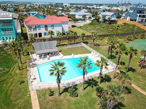 Um bairro residencial com piscina, cercado por palmeiras e um deck com grade.