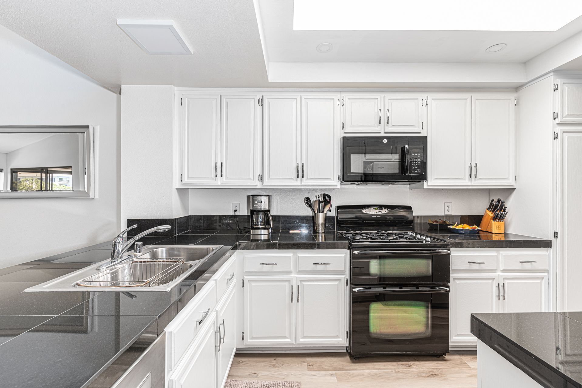 A modern kitchen with white cabinets, a black countertop, a built-in oven, a microwave, and a coffee maker.