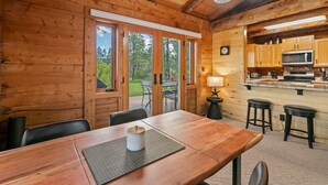 A wooden cabin interior with a dining table, chairs, a kitchen area, and a view of the outdoors. - Modern Log Cabin, Great Deck, 10 min from Durango! (Durango)