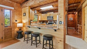 A wooden cabin interior with a kitchen featuring a large island, bar stools, and a view through the window. - Modern Log Cabin, Great Deck, 10 min from Durango! (Durango)