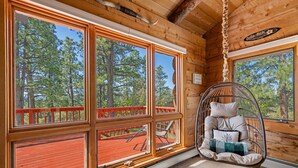 A wooden cabin with large windows, a red deck, and a hanging chair with cushions. - Modern Log Cabin, Great Deck, 10 min from Durango! (Durango)