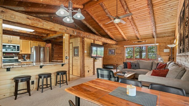 A cozy cabin interior with a wooden dining table, bar stools, a sofa, and a television. - Modern Log Cabin, Great Deck, 10 min from Durango! (Durango)