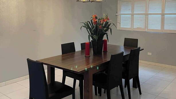 Een eetruimte met een houten tafel, zes stoelen, een kroonluchter en een bloeiende plant in pot.