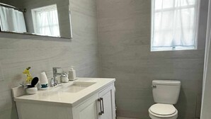 Een badkamer met een wit wastafelmeubel, een toilet en een raam met gordijnen.