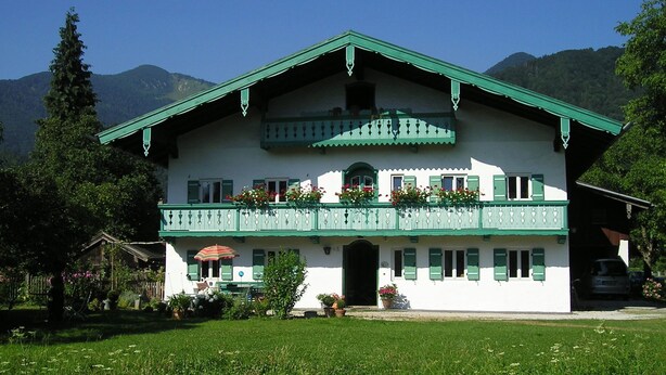 Ein zweistöckiges Gebäude mit grüner Dachbegrünung und Balkon, umgeben von einer Rasenfläche und Bäumen.