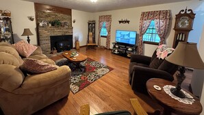 A cozy living room with a fireplace, comfortable seating, a television, and a clock on the wall.
