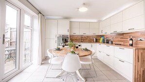 A modern kitchen with white cabinets, a wooden countertop, and a round dining table with white chairs. - Spindrift, Felixstowe (Felixstowe)