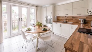 A modern kitchen with white cabinets, a wooden countertop, and a dining area with a table and chairs. - Spindrift, Felixstowe (Felixstowe)