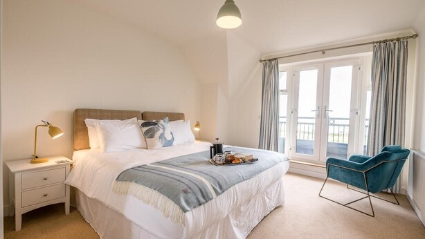 A bedroom with a bed, bedside tables, a lamp, a chair, and a window with curtains. - Spindrift, Felixstowe (Felixstowe)