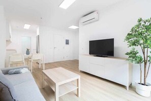 A modern living room with a flat-screen TV, a dining area with chairs, a sofa, a coffee table, and a potted plant.