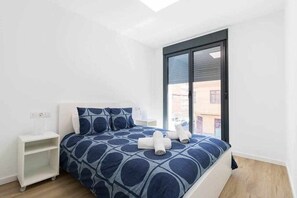 A bedroom with a bed, a nightstand, a window, and a view of buildings outside. - Arrecife Canteras Apartment (Palmas De Gran Canaria, Las)