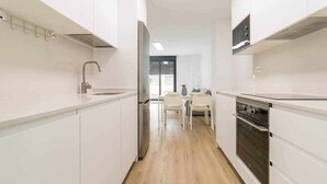 A modern kitchen with white cabinetry, a stainless steel refrigerator, a built-in oven, and a dining area with a table and chairs.