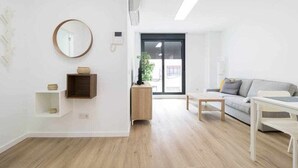 A modern living room with a wooden floor, a round mirror, a small wooden cabinet, a white sofa, and a coffee table.