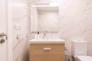 A bathroom with a marble wall, a sink with a mirror, a wooden cabinet, and a toilet. - Arrecife Canteras Apartment (Palmas De Gran Canaria, Las)