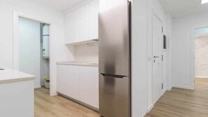 A modern kitchen with white cabinetry, a stainless steel refrigerator, and a wooden floor.