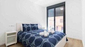 A modern hotel room with a large bed, a nightstand, and a window with a view of buildings.