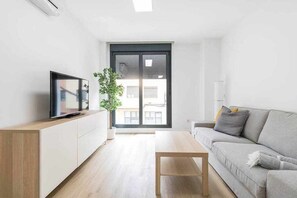 A modern living room with a sofa, a coffee table, a TV on a stand, and a potted plant. - Arrecife Canteras Apartment (Palmas De Gran Canaria, Las)