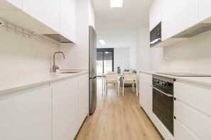 Een moderne keuken met witte kasten, een roestvrijstalen afzuigkap en een eethoek met een tafel en stoelen.