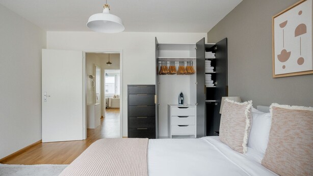 A bedroom with a bed, bedside table, wardrobe, and a hanging light fixture. - Superb Gellert 2 Room w/ Storage Room, nr Tram & Market, by Blueground (Basel)