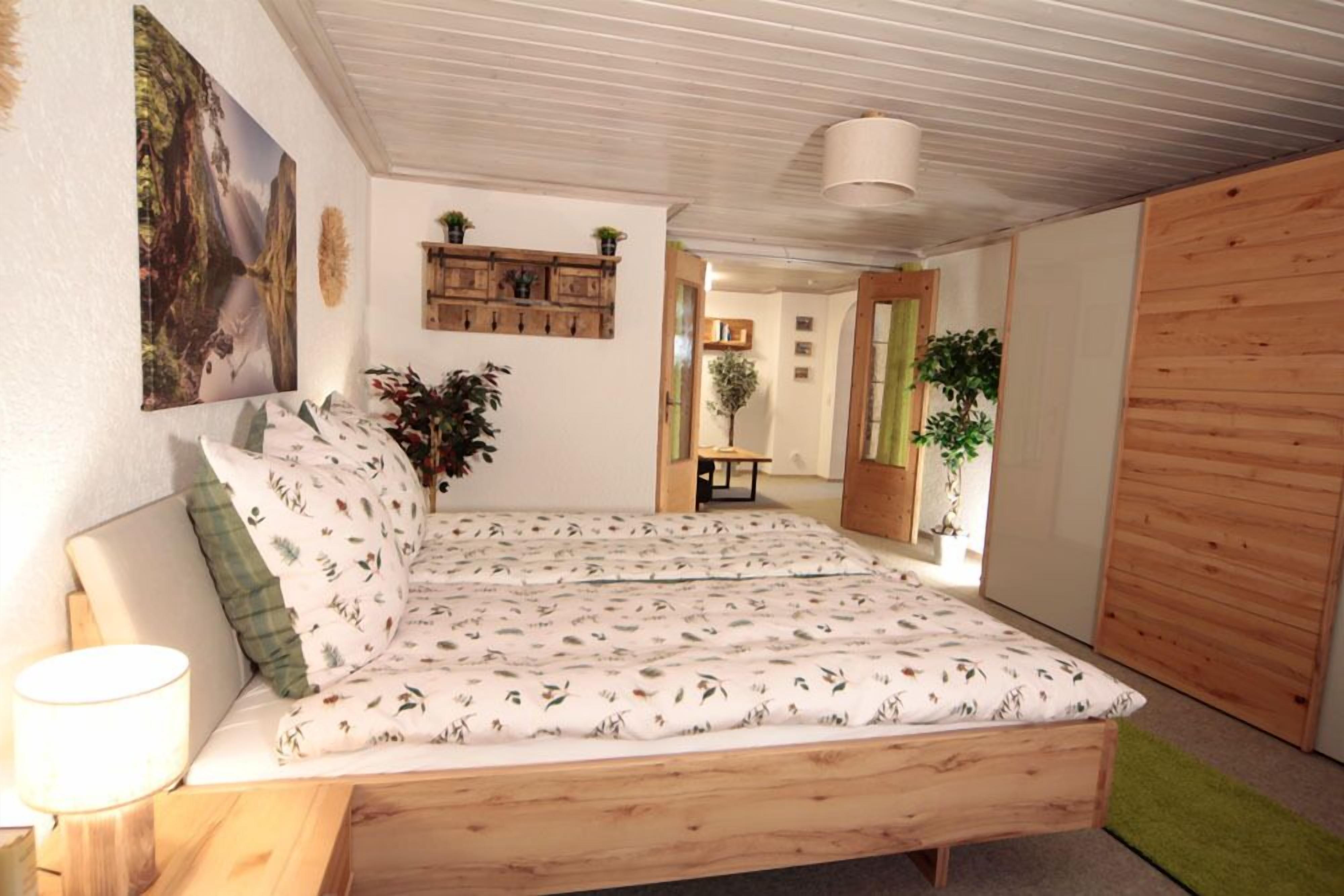 Ein Schlafzimmer mit einem hölzernen Bett, einem Nachttisch, einem Wandregal mit Pflanzen und einem Gemälde.