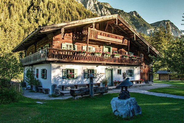 A traditional wooden chalet with a balcony, surrounded by a mountainous landscape.