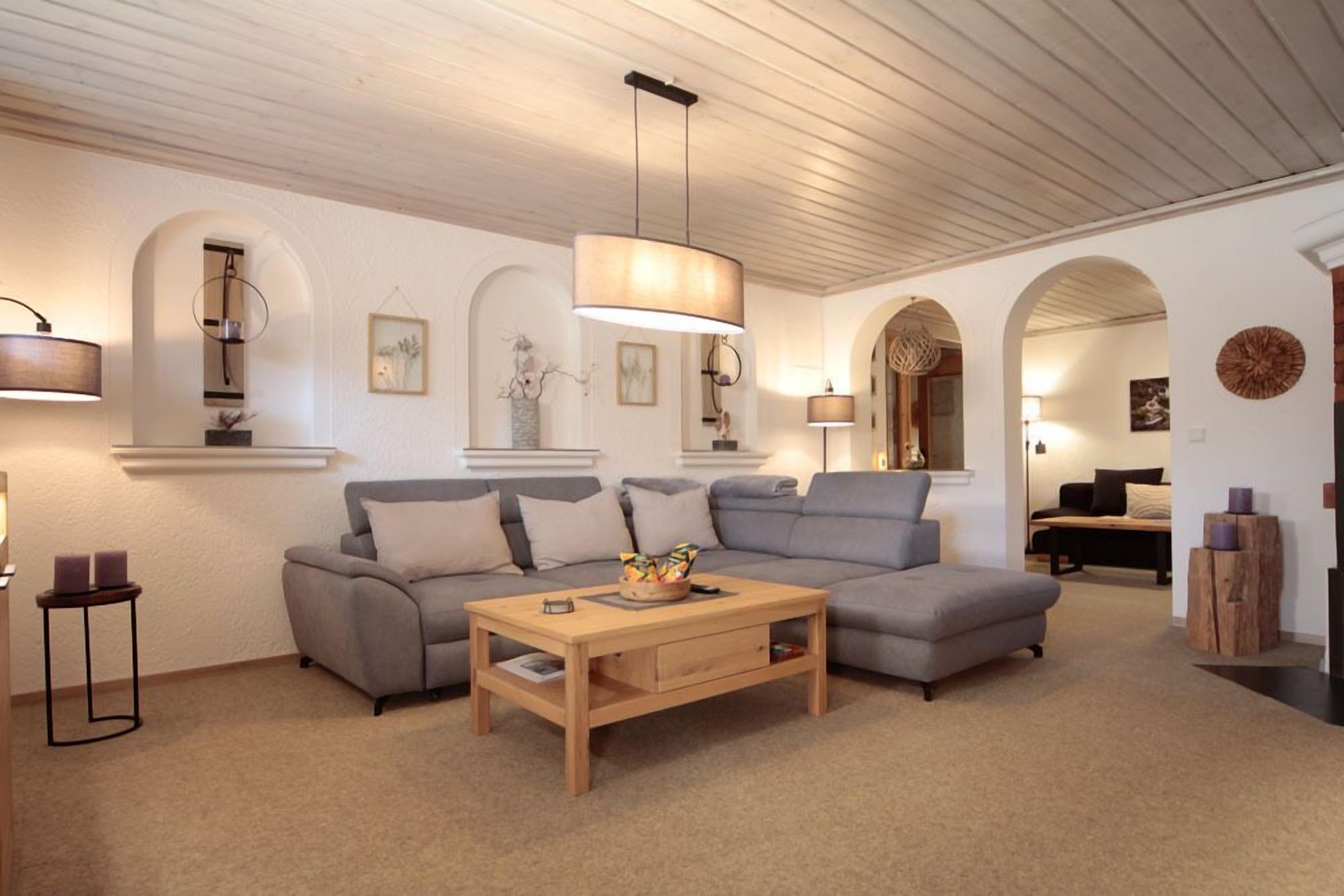 Ein gemütliches Wohnzimmer mit grauem Sofa, einem Holztisch und einer Pendelleuchte.