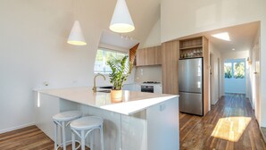 A modern kitchen with a central island, white bar stools, wooden flooring, and built-in appliances.