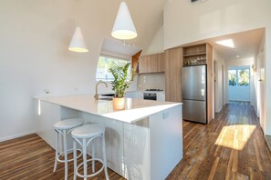 Cozinha moderna com ilha central, banquetas brancas, soalho de madeira e eletrodomésticos embutidos.
