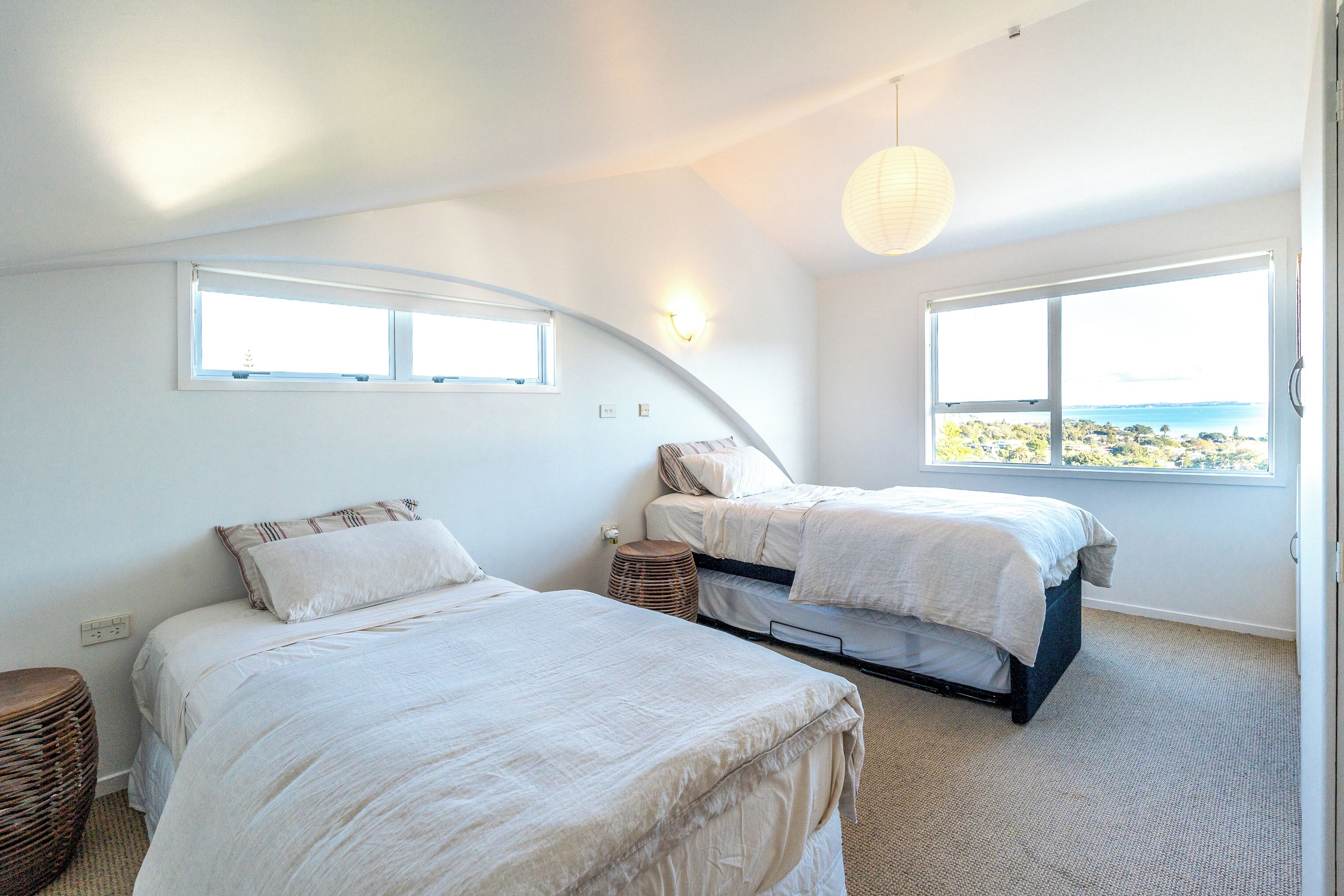 A bedroom with two beds, a large window, and a view of the sea.