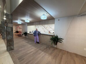 Zona de recepción con pared de mármol, mostrador de recepción y diseño moderno en el techo.