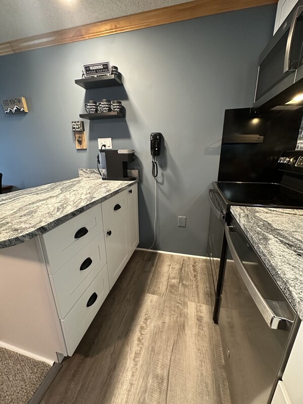 A kitchen with a granite countertop, white cabinetry, a black stove, and a phone mounted on the wall. - Mountain Lodge #327! Remodeled kitchen! Only yards away from Ballhooter lift! (Snowshoe)