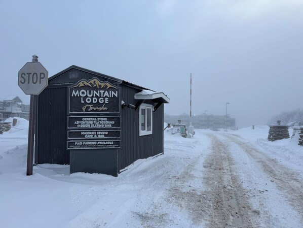Letrero nevado de Mountain Lodge en Snowshoe, que enumera servicios como una tienda general, parque de aventuras, pista de patinaje interior, estudio de masajes, cafetería y bar, y estacionamiento de pago.