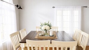 Een eetkamer met een houten tafel, witte stoelen, een vaas met bloemen en een kaars.