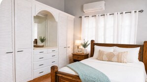 Een slaapkamer met een houten bed, witte gordijnen, een nachtkastje en een kledingkast met schuifdeuren.