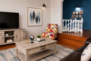 A living room with a TV, a coffee table, a chair, a sofa, and a staircase.