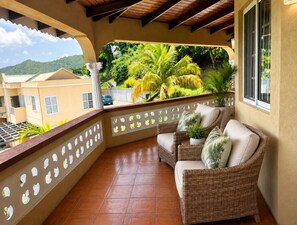 A balcony with wicker furniture, a view of a mountain, and a car parked outside.